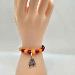 May include: A red, yellow, and white beaded bracelet with a silver charm shaped like a flame.