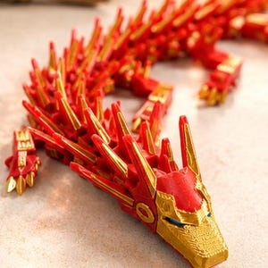 May include: A red and gold articulated dragon figurine. The dragon has a detailed design with sharp, gold-colored spikes along its back and head. The head features intricate gold accents and blue eyes.