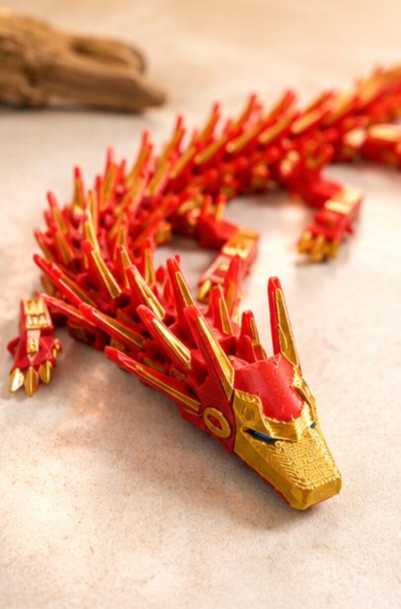 May include: A red and gold articulated dragon figurine. The dragon has a detailed design with sharp, gold-colored spikes along its back and head. The head features intricate gold accents and blue eyes.