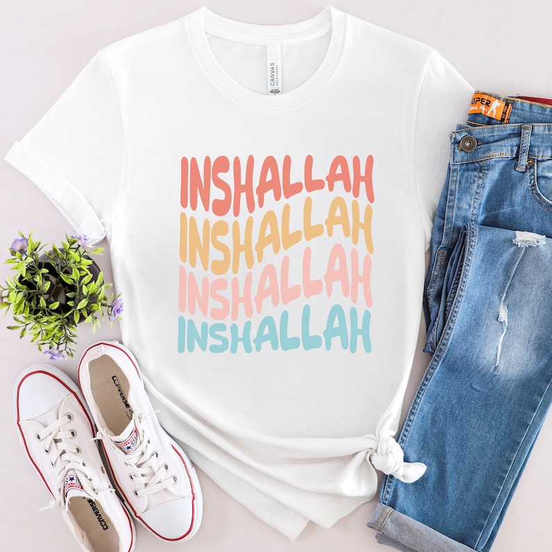May include: White t-shirt with the phrase "Inshallah" repeated four times in a rainbow gradient. The text is in a retro font style.