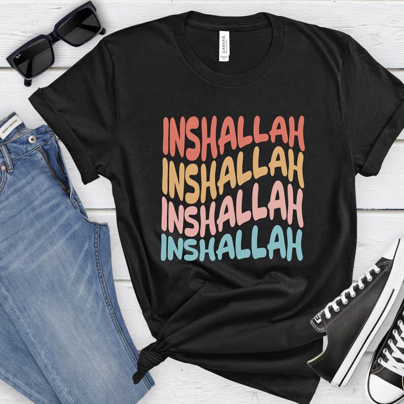 May include: Black t-shirt with the phrase "Inshallah" repeated four times in a rainbow color gradient. The text is in a bold, stylized font.
