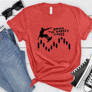 May include: Red t-shirt with a black silhouette of a person surfing on a candlestick chart. The text "Riding the Market Waves" is printed on the shirt.
