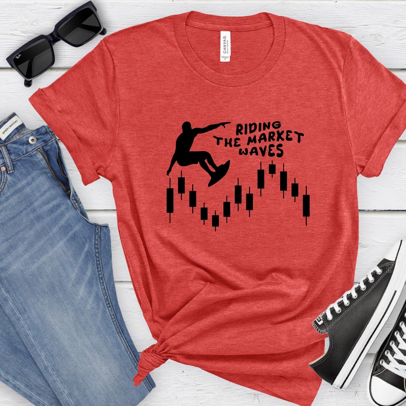 May include: Red t-shirt with a black silhouette of a person surfing on a candlestick chart. The text "Riding the Market Waves" is printed on the shirt.