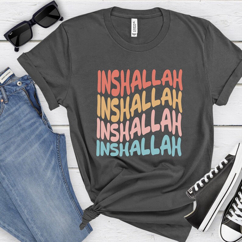 May include: A dark gray t-shirt with the word "Inshallah" repeated four times in a rainbow color scheme. The text is in a bold, handwritten style.