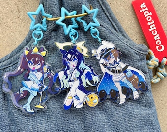 Könnte beinhalten: Drei Schlüsselanhänger mit Anime-Charakteren und blauen sternförmigen Anhängern. Die Charaktere haben lange Haare und tragen farbenfrohe Outfits. Ein Schlüsselanhänger hat ein rotes Etikett mit der Aufschrift "Coachtopia". Die Schlüsselanhänger befinden sich auf einem Jeans-Hintergrund.