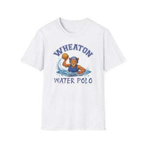 May include: A white short-sleeve t-shirt featuring a graphic of a lion wearing a blue water polo cap and swimming in water while holding a yellow ball. The text WHEATON is arched above the lion, and WATER POLO is printed below in blue letters.