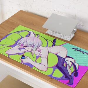 以下が含まれることがあります： ライトパープルの髪の人物がライターを持っているアニメスタイルのイラストが描かれた長方形のマウスパッド。マウスパッドは、"Cyberpunk"のテキストが入った緑と紫の背景です。背景にはラップトップとキーボードが見えます。