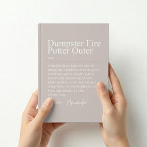 May include: A light taupe notebook featuring white text that reads: Dumpster Fire Putter Outer, noun. Someone who thrives under pressure, stepping in with quick thinking and a steady hand whenever things get hard. Resourceful and unshakable.