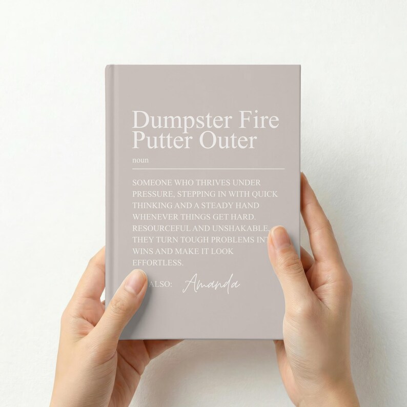 May include: A light taupe notebook featuring white text that reads: Dumpster Fire Putter Outer, noun. Someone who thrives under pressure, stepping in with quick thinking and a steady hand whenever things get hard. Resourceful and unshakable.