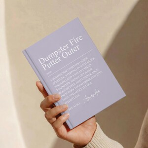 May include: A light purple hardcover journal featuring the white printed text Dumpster Fire Putter Outer, followed by a dictionary-style definition and the name Amanda. The book cover has a matte finish and displays a clean, modern layout.