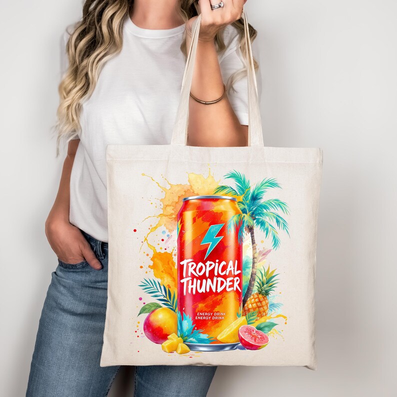 A woman is holding a tote bag with a colorful illustration of a can of Tropical Thunder energy drink surrounded by tropical fruits such as pineapple, mango, and orange.