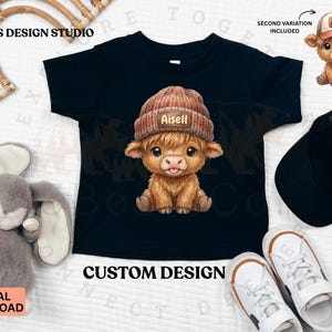 May include: Black t-shirt featuring a cartoon Highland cow wearing a brown knit cap with the name "Aisell". The image includes a second variation of the cow wearing a baseball cap. Text on the shirt reads "CUSTOM DESIGN".