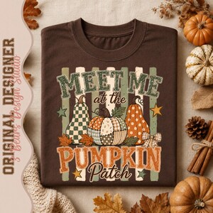 May include: A dark brown t-shirt featuring a graphic print with the text "MEET ME at the PUMPKIN Patch". The design includes three pumpkins with checkered, polka dot, and floral patterns, surrounded by vertical stripes, stars, and leaves.