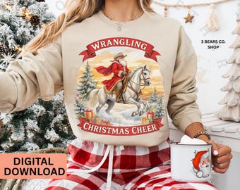 May include: Beige sweatshirt with a graphic of Santa Claus riding a white horse, with the words "Wrangling Christmas Cheer." The design includes Christmas trees and gift boxes. The words "Digital Download" are also visible.