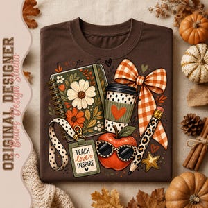Könnte beinhalten: Ein dunkelbraunes T-Shirt mit einem Grafikdruck aus einem Spiralnotizbuch, einem Kaffeebecher, einem roten Apfel mit Sonnenbrille, einem Bleistift und einem Schlüsselband mit einem Schild, auf dem "TEACH love INSPIRE" steht, sowie einer orangefarbenen Vichy-Schleife.