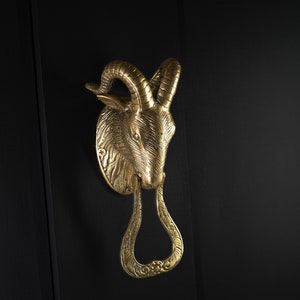 May include: A gold-toned door knocker shaped like a ram's head with a decorative ring.