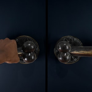 Puede incluir: Un par de manillas de puerta con un diseño único. Las manillas son de latón y tienen un acabado oscuro. Una manija está siendo agarrada por una mano.