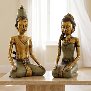 Op de afbeelding: Twee beelden van zittende figuren, één met een hoge puntige hoofdtooi en één met een versierd kapsel. Beide figuren hebben goudkleurige bovenlichamen en gedempt groene onderkleding met gedetailleerde afwerking, in een knielende houding.