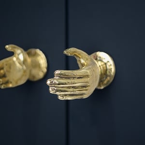 Peut inclure: Deux poignées de porte en forme de main dorées sur un fond bleu foncé.