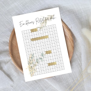 Può includere: Un biglietto bianco con un disegno floreale marrone e verde. Il biglietto ha un cruciverba con il testo "Ein kleines Rätsel für dich..." in alto.