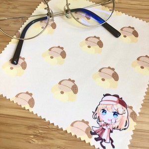 May include: A white microfiber cleaning cloth with a repeating pattern of cartoon dogs wearing hats. A pair of round, gold-rimmed glasses with blue lenses is lying on top of the cloth. A small cartoon character wearing a brown hat and coat is printed on the cloth.