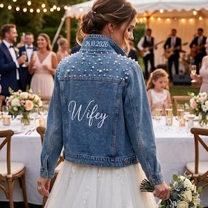 Könnte beinhalten: Eine Jeansjacke mit Perlenbesatz und dem gestickten Wort "Wifey" auf dem Rücken. Das Datum "26.10.2026" ist ebenfalls auf dem Kragen zu sehen. Die Jacke wird auf einer Hochzeit getragen.