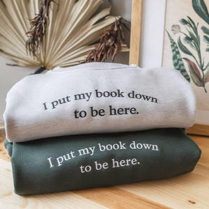 Jag lägger ner min bok för att vara här broderad tröja, bokälskare rund hals, rolig läsarcitattröja, mysig litterär tröja, introvert gåva