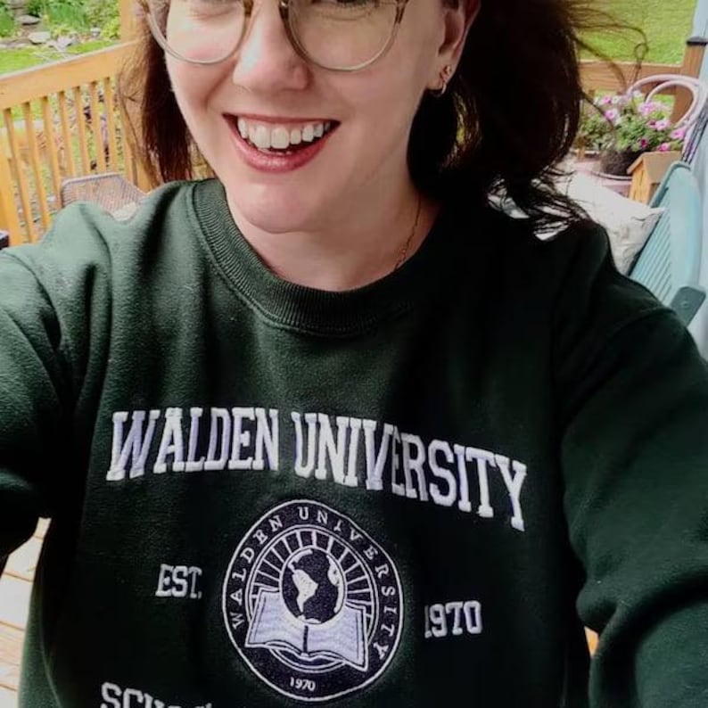 Puede incluir: Sudadera verde oscuro con el texto blanco "WALDEN UNIVERSITY". Debajo, un emblema circular con "WALDEN UNIVERSITY" y "EST. 1970". La sudadera es de cuello redondo.