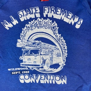 May include: A blue sweatshirt with a white print of a fire truck and the text "N.J. STATE FIREMEN'S WILDWOOD, N.J SEPT. 1989 CONVENTION"