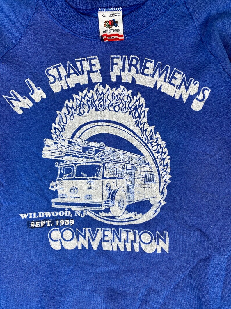 May include: A blue sweatshirt with a white print of a fire truck and the text "N.J. STATE FIREMEN'S WILDWOOD, N.J SEPT. 1989 CONVENTION"