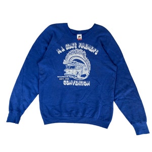 May include: Blue sweatshirt with a white graphic of a fire truck and the text "N.J. State Firemen's Convention" with the location and date "Wildwood, N.J. Sept. 1989"