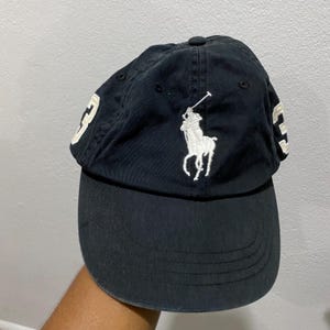 May include: Black baseball cap with a curved brim. Features a white embroidered polo player logo on the front and the number "3" on the side. The cap is made of a soft, worn fabric.