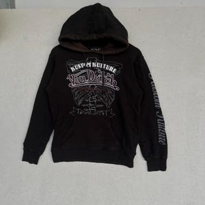 May include: A black hooded sweatshirt featuring a brown inner hood lining and a front graphic print that reads KUSTOM KULTURE VON DUTCH MOTORS. The design includes a skeletal rib cage illustration and the text KUSTOM KULTURE on the left sleeve.