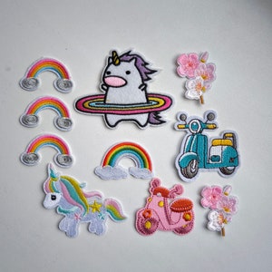 Op de afbeelding: Een set van tien strijkbare patches met een eenhoorn, regenbogen, een scooter en kersenbloesems. De patches zijn kleurrijk en fantasierijk, perfect om kleding, tassen of andere accessoires een persoonlijk tintje te geven.