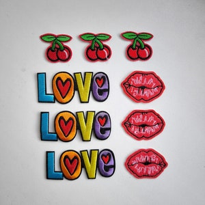 Op de afbeelding: Drie geborduurde strijkpatches met het woord "LOVE" in regenboogkleuren en drie rode geborduurde strijkpatches met een lippenmotief.