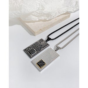 Puede incluir: Dos collares de plata con colgantes rectangulares negros y plateados. Los colgantes presentan un diseño de placa de circuito con las palabras "Forever Love" repetidas en cada uno.