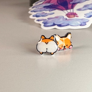 May include: A pair of small, colourful, cartoon dog earrings. One earring features a dog's face with a tongue sticking out, and the other earring features a dog's rear end.