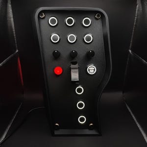 May include: Black control panel with multiple white-rimmed buttons, knobs, and a toggle switch. A red illuminated button and an "ENGINE START STOP" button are also visible. The panel has a curved design and is likely for a vehicle or machine.