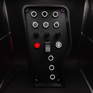 Könnte beinhalten: Schwarzes Bedienfeld mit mehreren Knöpfen und Schaltern. Es verfügt über beleuchtete weiße Kreise, einen roten Knopf und einen "ENGINE START STOP"-Knopf. Das Panel hat eine strukturierte Oberfläche und lila Akzente.