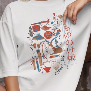 May include: A white t-shirt with a colorful graphic print of various objects and characters from the animated film "Spirited Away". The Japanese text on the shirt reads "もののけ姫".
