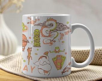 Pode incluir: Caneca de cerâmica branca com um design colorido que apresenta ilustrações de inspiração japonesa de um dragão, um sapo, uma nuvem, uma flor de cerejeira e um homem com um pano de renda. A caneca tem uma alça preta.