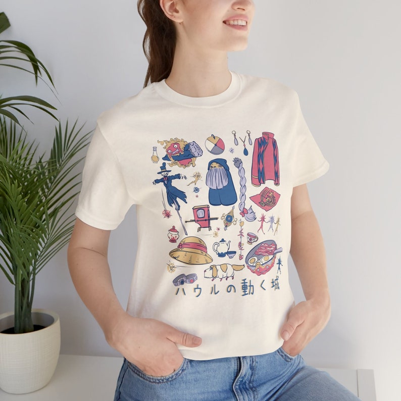 May include: A white t-shirt with a colorful graphic print of various characters and objects from the movie Howl's Moving Castle. The text "ハウル の 動く 城" is printed in Japanese at the bottom of the shirt.