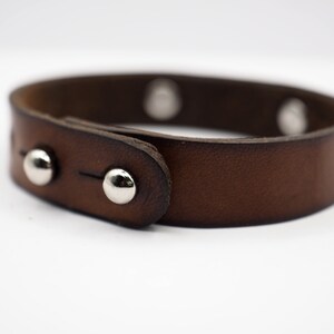 Op de afbeelding: Een bruin leren armband met zilveren studs. De armband heeft een gespsluiting.