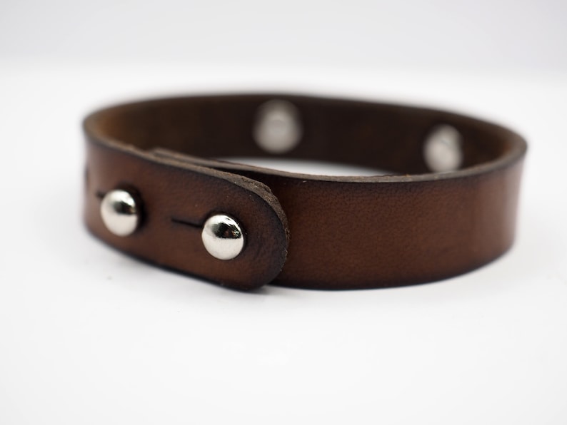 Op de afbeelding: Een bruin leren armband met zilveren studs. De armband heeft een gespsluiting.