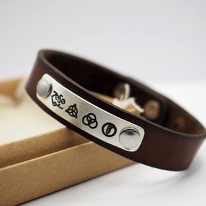 Könnte beinhalten: Braunes Lederarmband mit einer silbernen Platte, die mit den Symbolen der Band Led Zeppelin graviert ist. Das Armband hat zwei silberne Nieten.