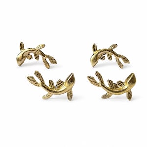 May include: Four gold-colored metal fish-shaped stud earrings. Each earring features a textured surface with detailed fins and a curved body design. The fish are arranged in two pairs, showing the front-facing side of each individual piece.
