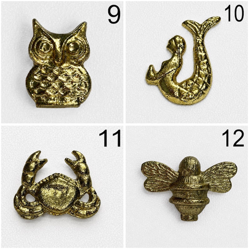 May include: A collection of four gold-toned metal charms labelled 9 through 12. The charms feature an owl, a mermaid, a crab, and a bee. Each piece has a textured, metallic finish and is displayed against a plain, light-coloured background.