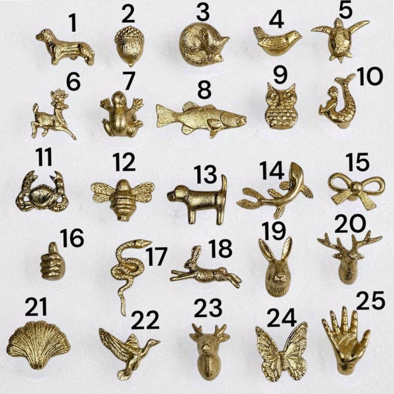 May include: A collection of twenty-five small gold-toned metal charms arranged in a grid, each numbered from 1 to 25. The charms feature various shapes including animals like a dog, owl, fish, and turtle, as well as objects like a bow, shell, and hand.