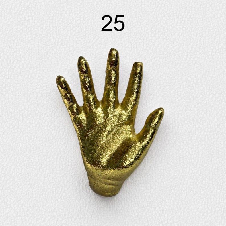 May include: A gold-coloured, textured hand-shaped sculpture with five fingers extended, featuring a metallic finish and a rough, organic surface. The number 25 is printed in black above the hand-shaped object, which is displayed on a white surface.