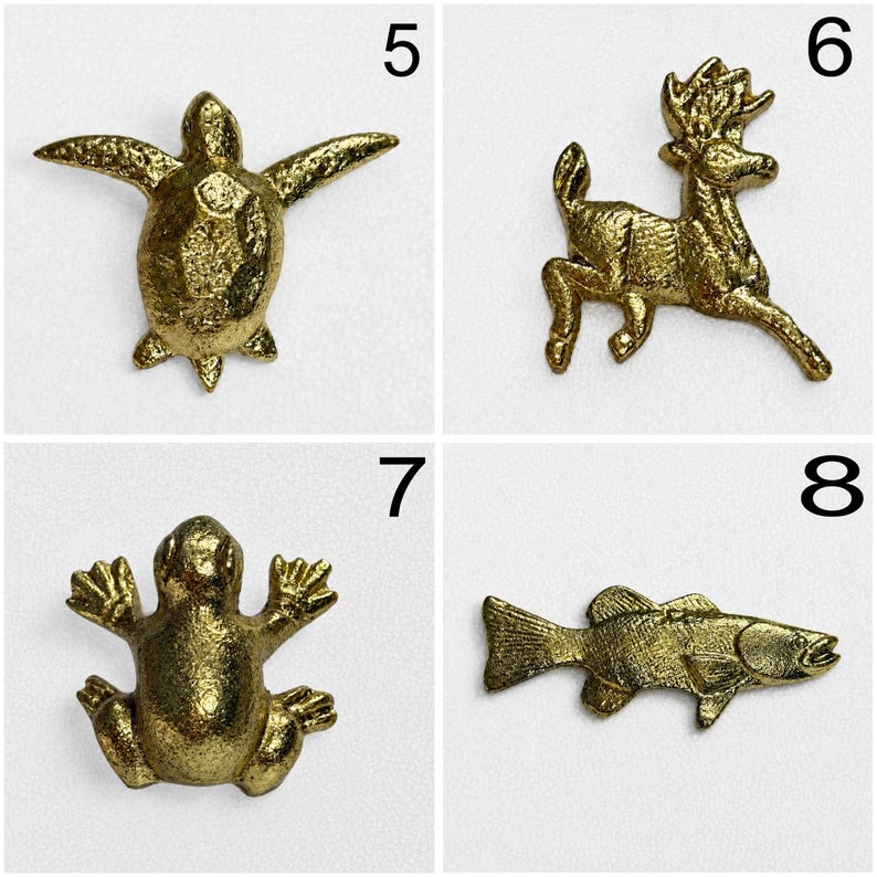 May include: A collection of four gold-toned metal animal-shaped pins or charms. The set includes a sea turtle labelled 5, a deer labelled 6, a frog labelled 7, and a fish labelled 8. Each piece features a textured, metallic finish and distinct details.